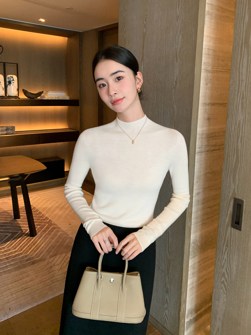Woman wearing a white long-sleeve top with a black skirt and beige handbag