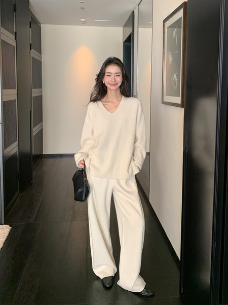 Woman wearing a cream knit sweater with matching wide-leg pants and black bag