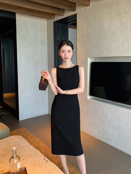 Woman wearing a black sleeveless midi dress and holding a small handbag