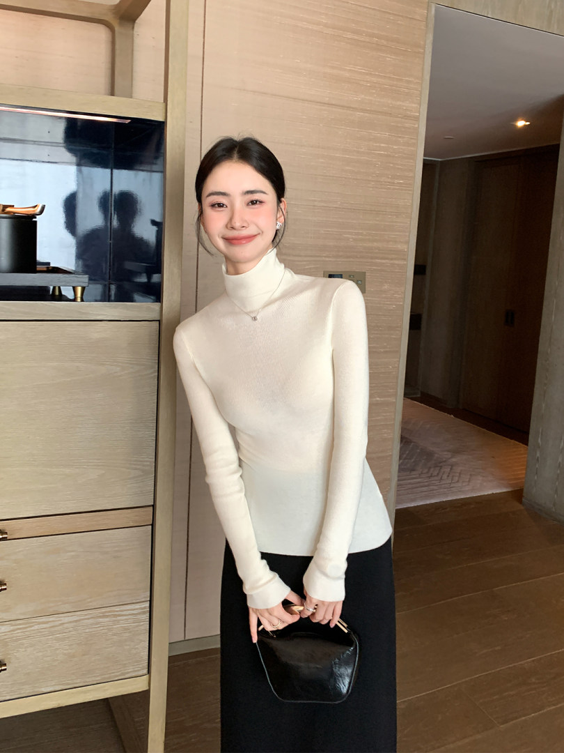 Woman wearing a cream turtleneck top with a black skirt and black handbag
