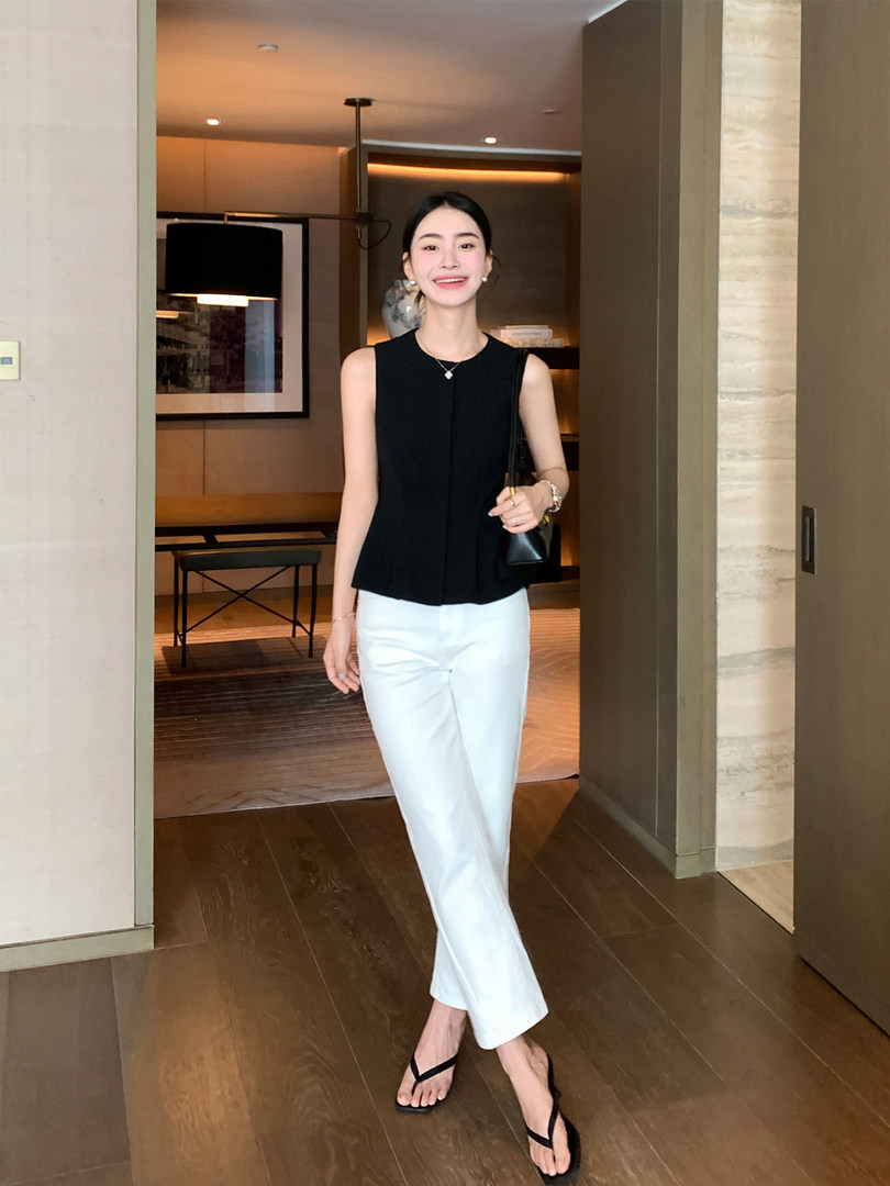 Model wearing a black sleeveless top with white trousers and black flip-flop sandals