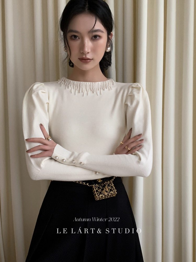 Model wearing a cream embellished long-sleeve top with a black skirt