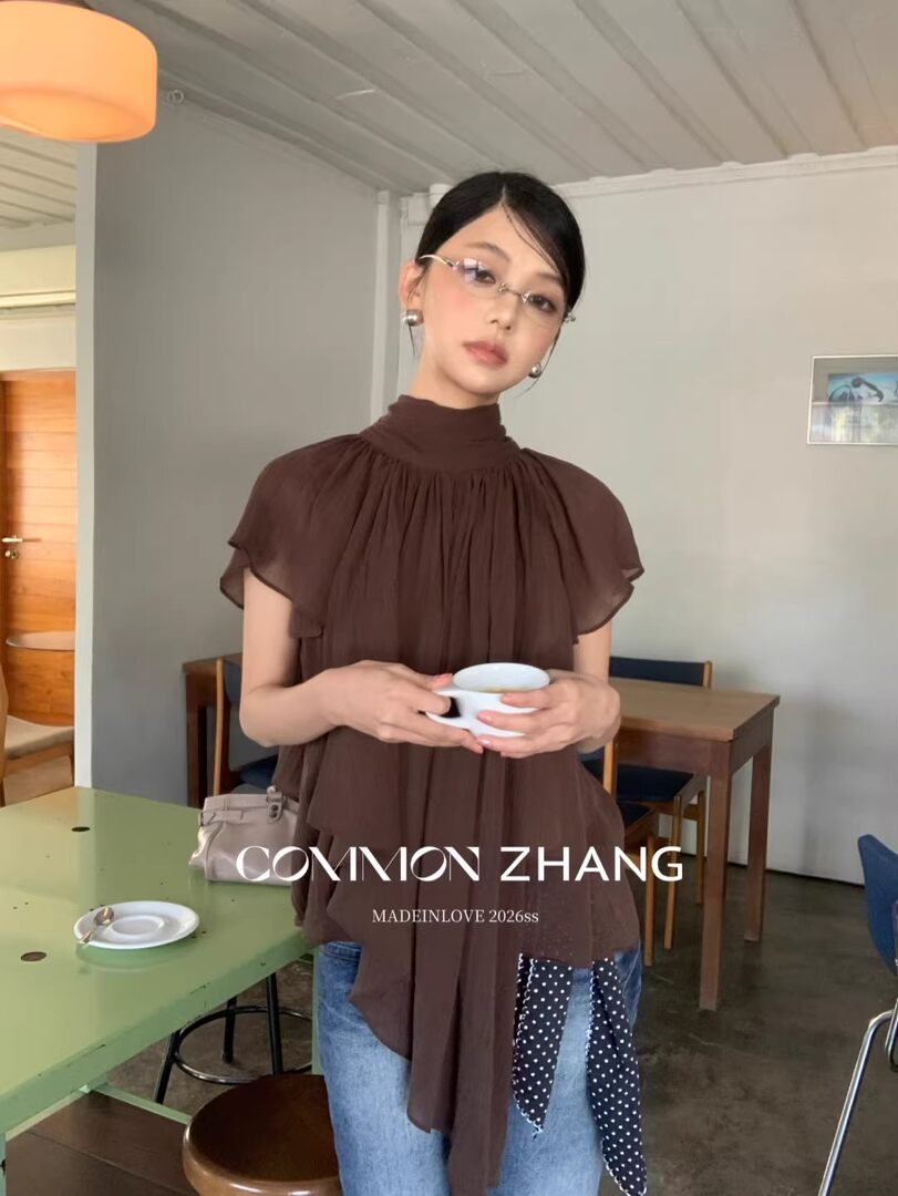 Model wearing a brown sheer high-neck blouse with a draped tie detail