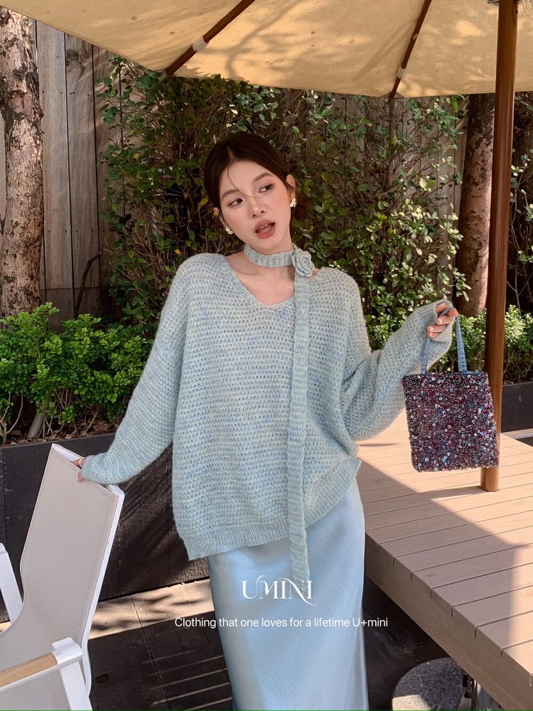 Model wearing a light blue knit sweater and skirt set outdoors while holding a small handbag