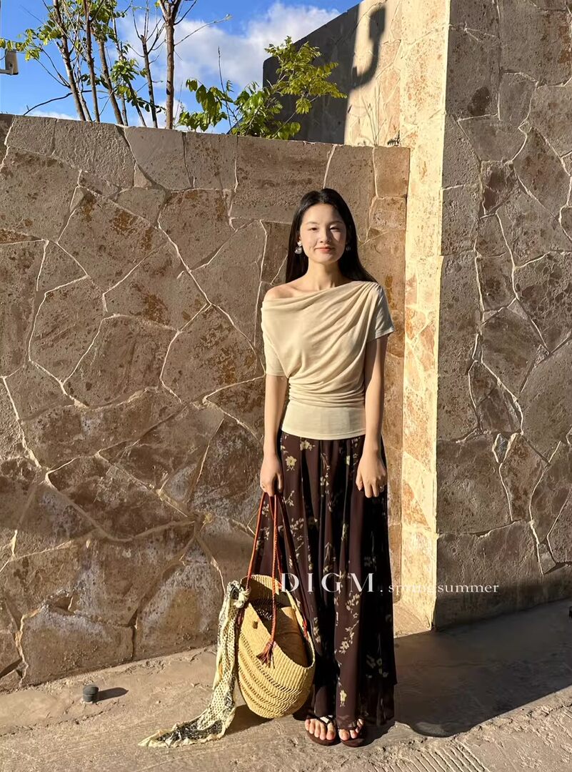 Woman wearing a beige draped top with a floral maxi skirt and woven straw bag