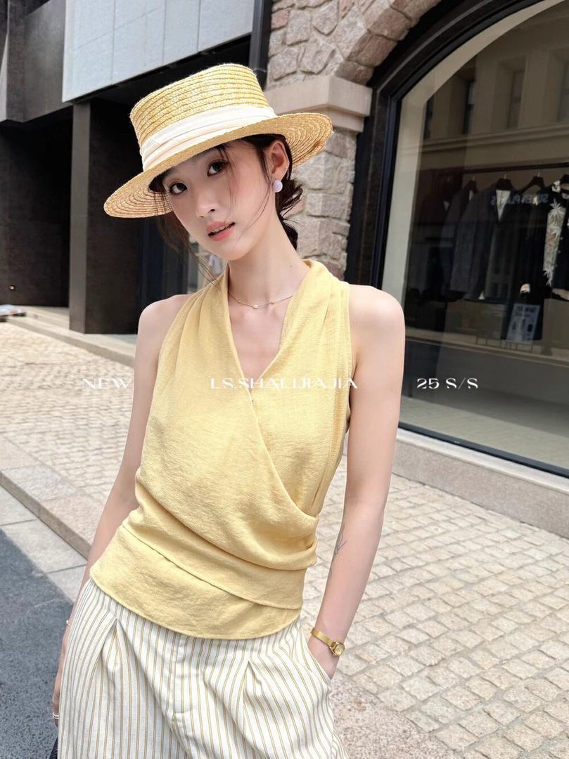 Woman wearing a yellow sleeveless wrap top and straw hat outdoors