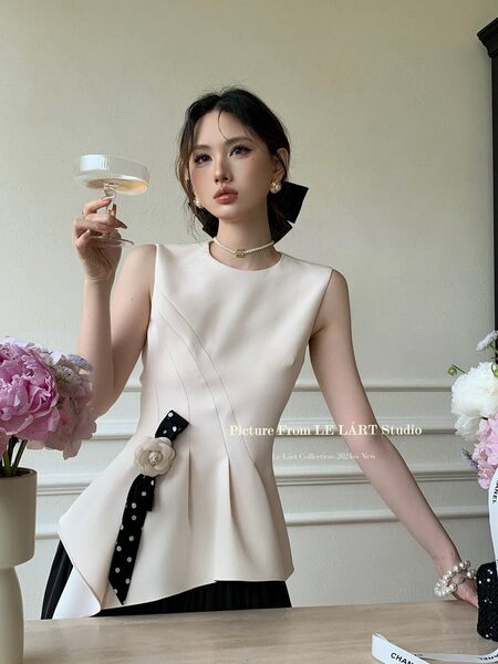 Model wearing a cream sleeveless dress with black ribbon detail