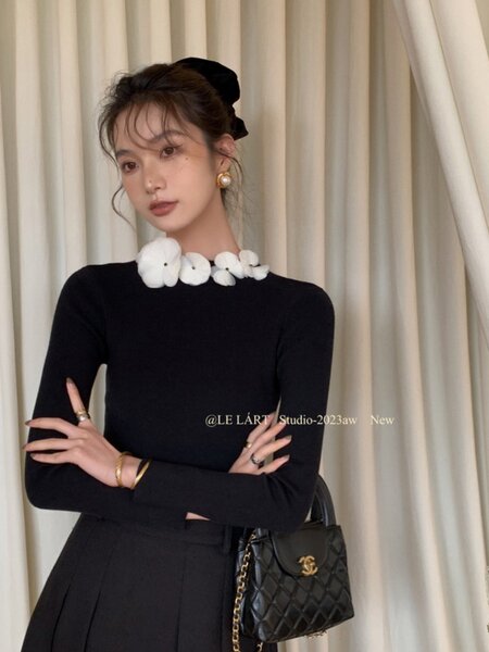 Black long-sleeve dress worn by a model with a floral collar and black handbag