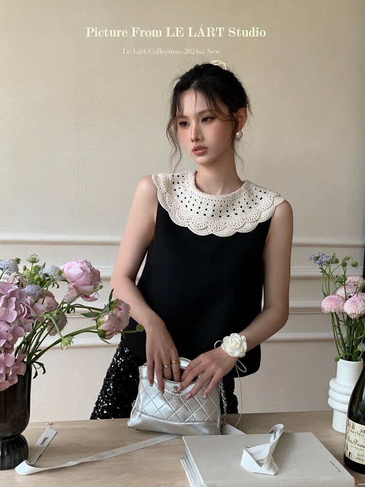 Model wearing a black sleeveless top with a white lace collar, styled with a metallic silver handbag