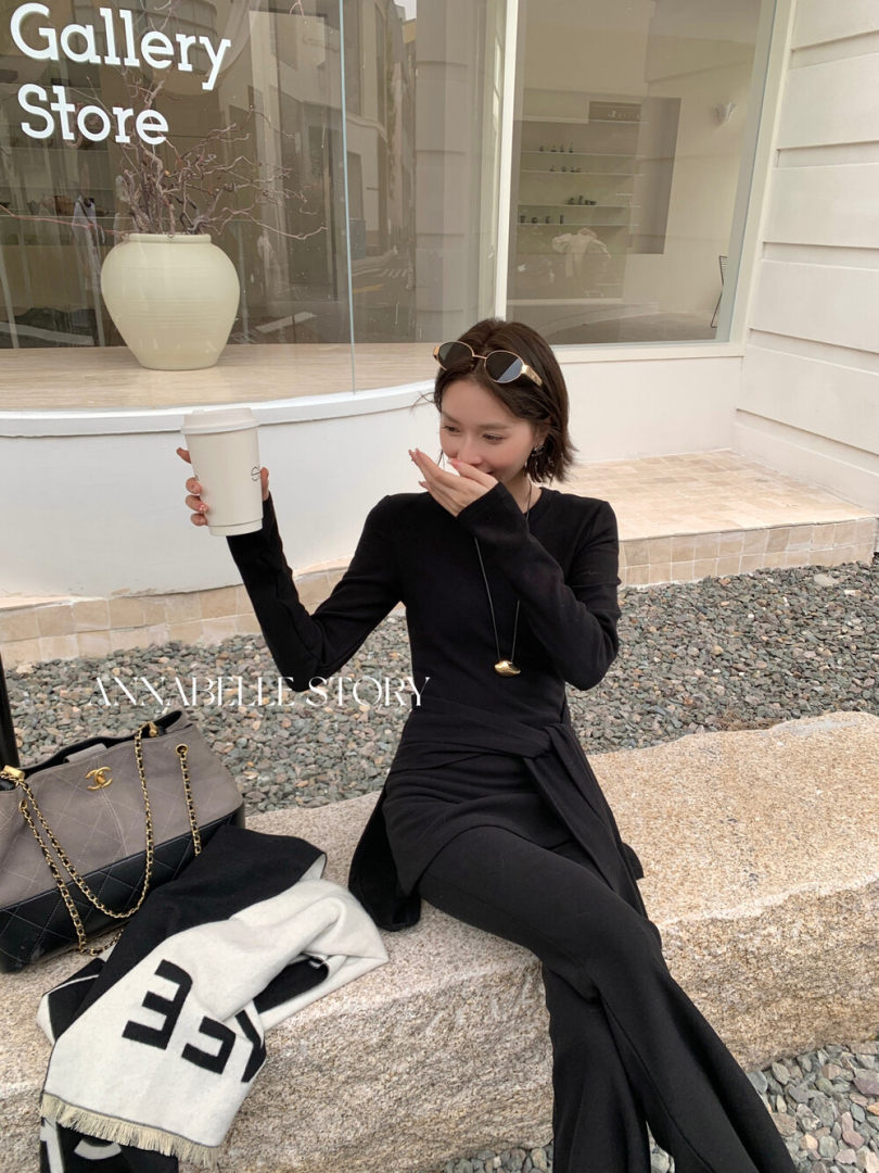 Woman wearing a black long-sleeve outfit sitting outdoors with a handbag and coffee cup