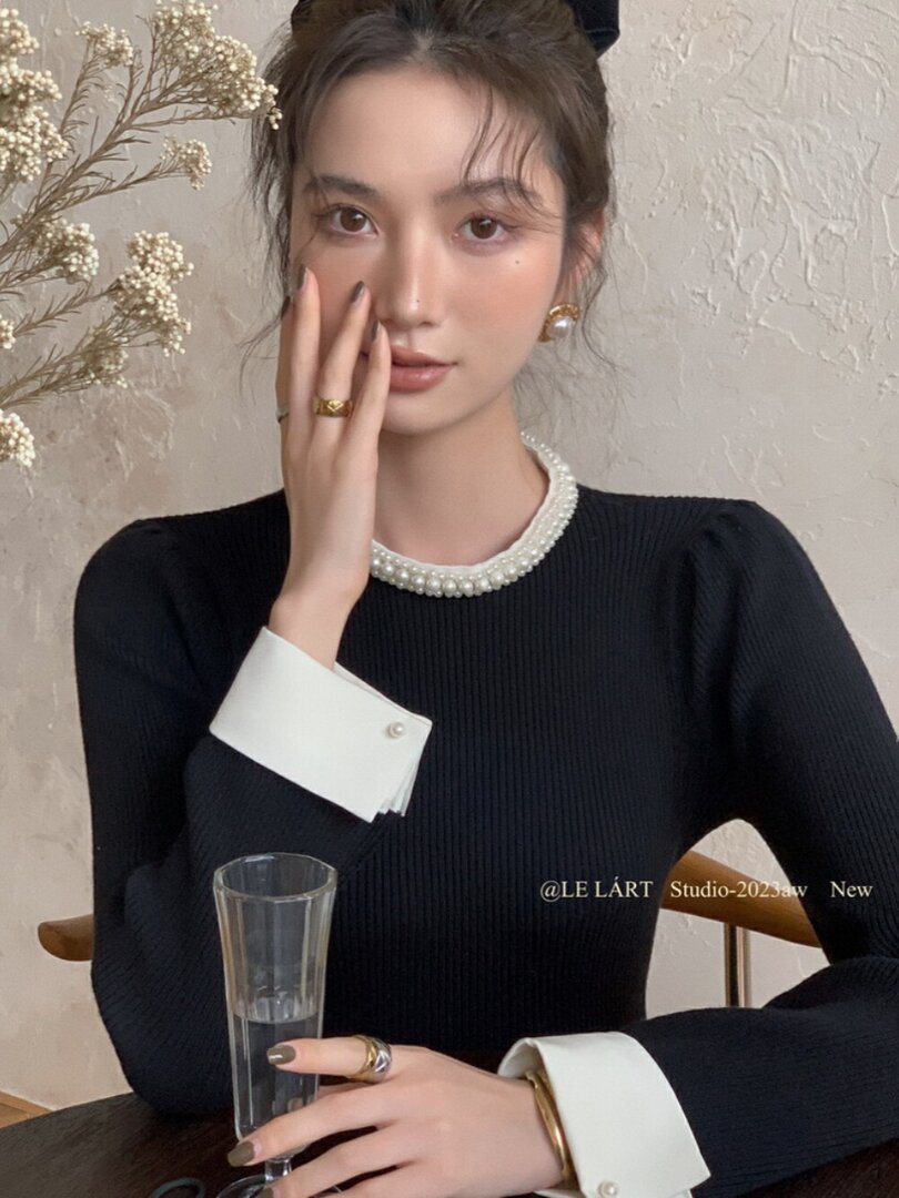 Black long-sleeve knit top with pearl-trim collar and white cuffs worn by a model