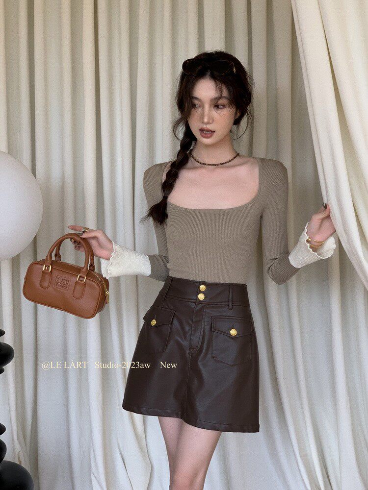 Woman wearing a fitted long-sleeve top and faux leather mini skirt while holding a small brown handbag