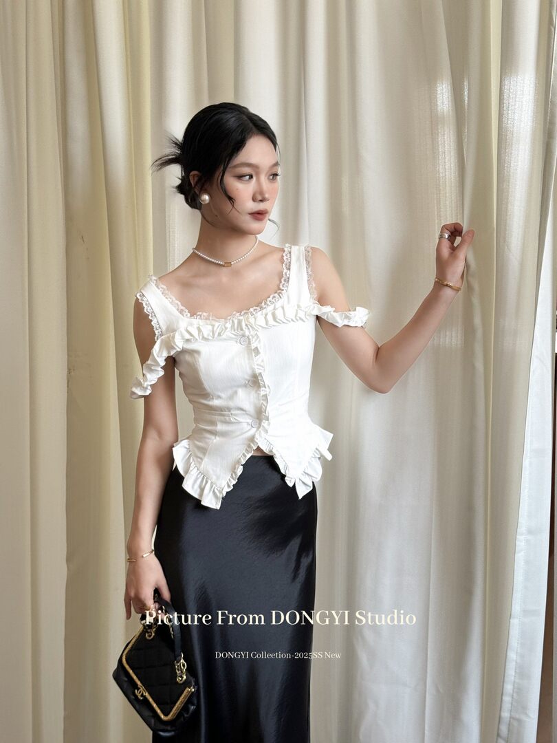 Woman modeling a white ruffled sleeveless top with a black skirt and handbag