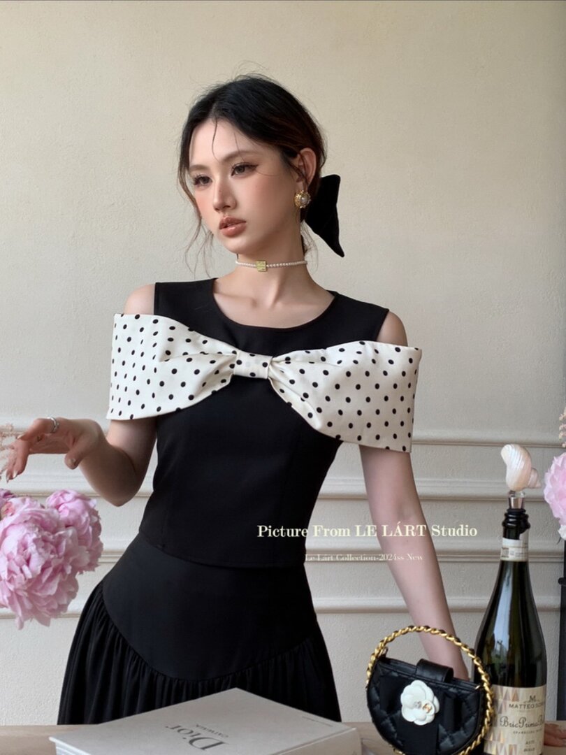 Black sleeveless dress with oversized white polka dot bow detail worn by a model