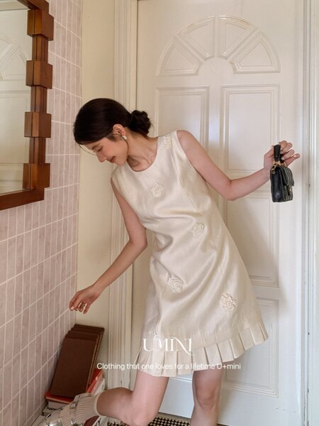 Woman wearing a cream sleeveless mini dress with pleated hem