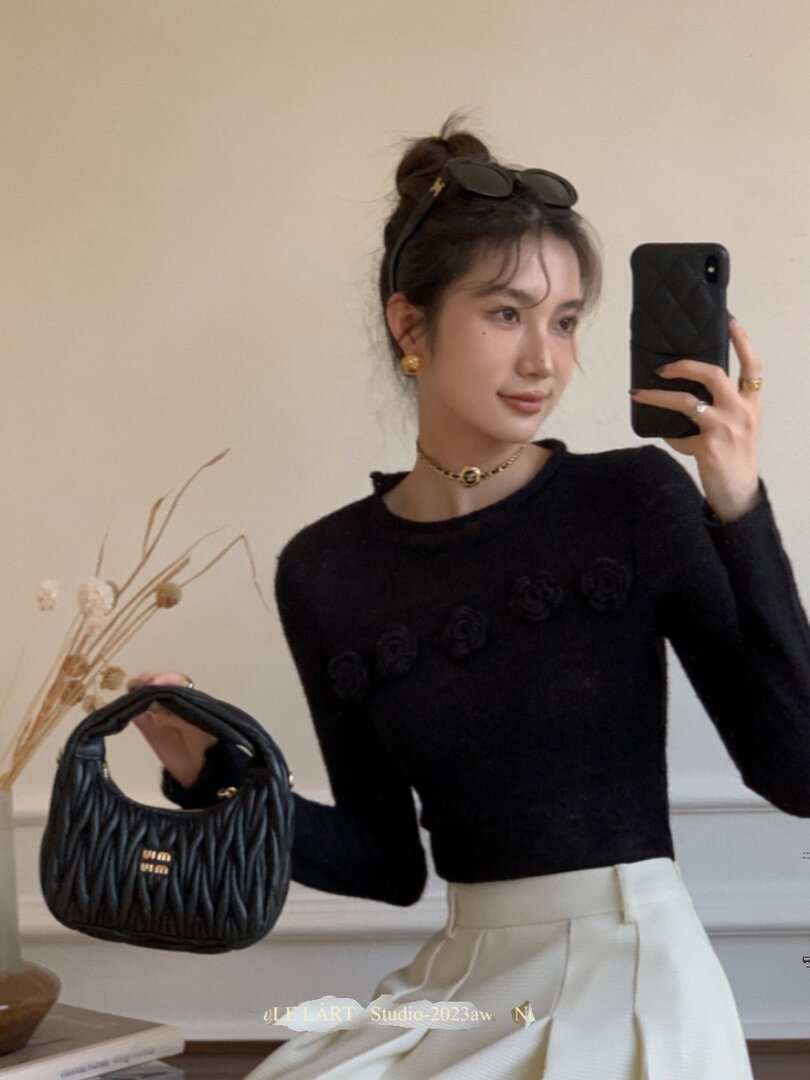 Woman modeling a black long-sleeve top with a black handbag and white skirt
