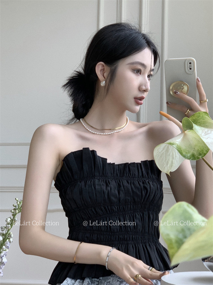 Black strapless ruched top worn by a model taking a mirror selfie