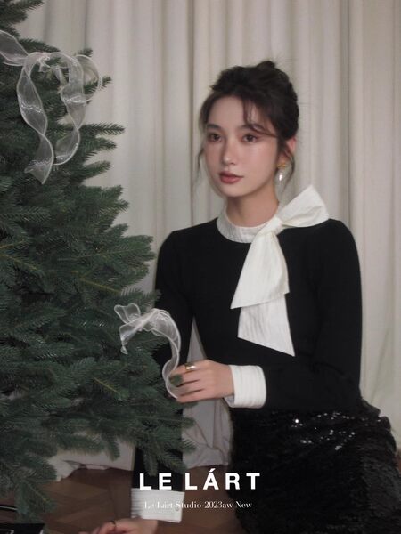 Black long-sleeve top worn by a model, styled with a white bow neck detail
