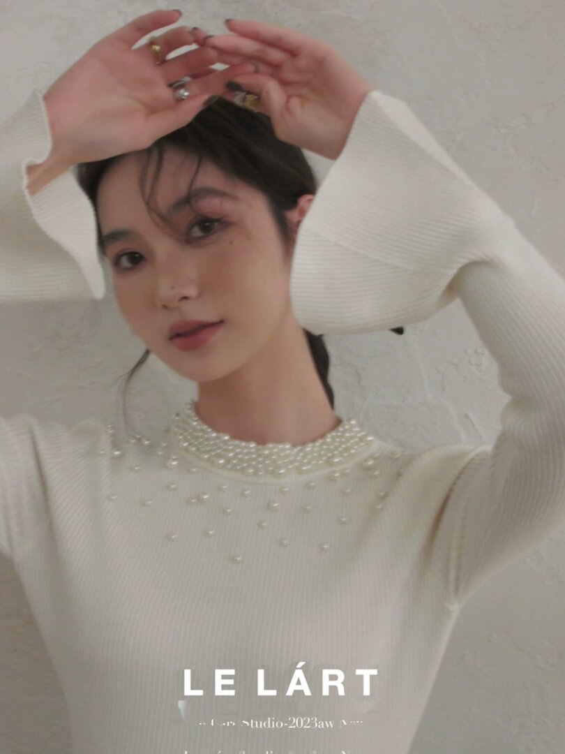 Model wearing a white ribbed knit top with pearl embellishments