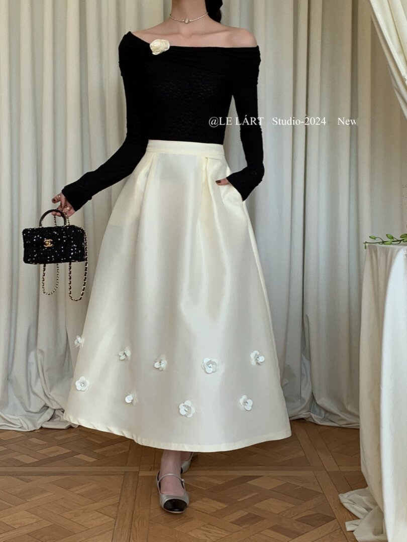 Model wearing a black off-shoulder top with a cream floral midi skirt and handbag