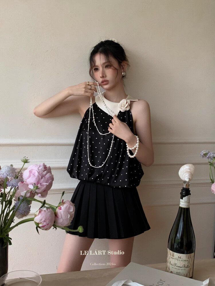 Model wearing a black polka dot sleeveless top with a pleated mini skirt