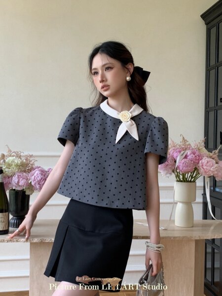 Model wearing a dark polka dot blouse with a white collar bow and black skirt