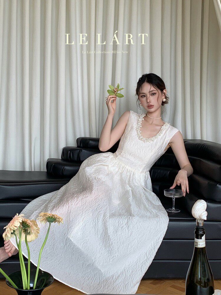 Model wearing a sleeveless white formal dress seated on a black sofa