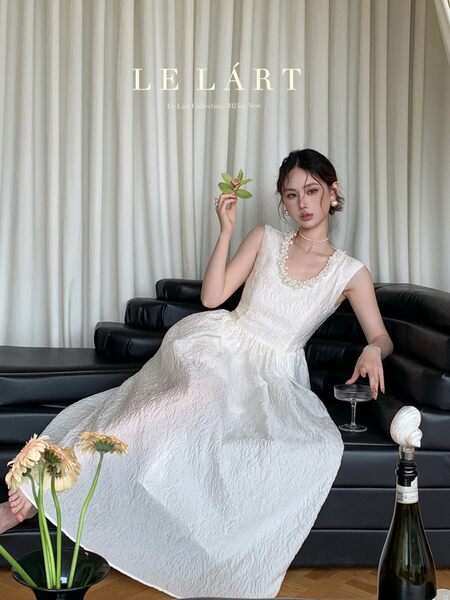 Model wearing a sleeveless white formal dress seated on a black sofa