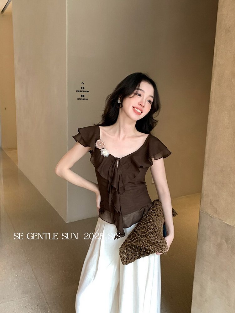 Model wearing a brown ruffled sheer blouse with white pants