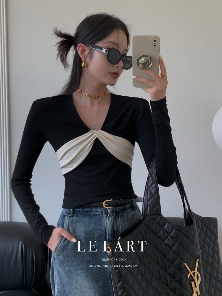 Woman wearing a black long-sleeve top with cream draped front detail and a quilted black tote bag.