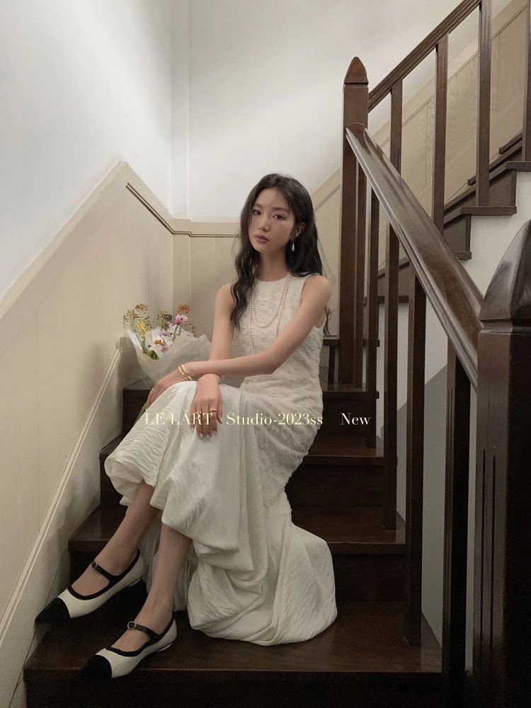 Woman wearing a white sleeveless dress and black-and-white shoes on a staircase