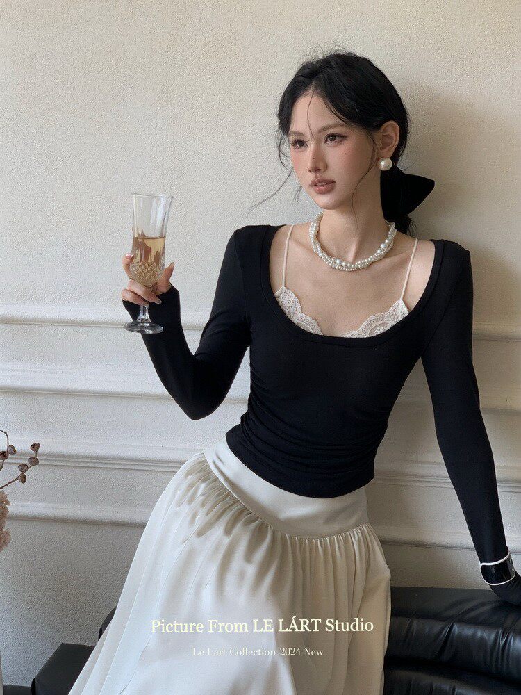 Woman modeling a black fitted top with a white skirt and pearl accessories
