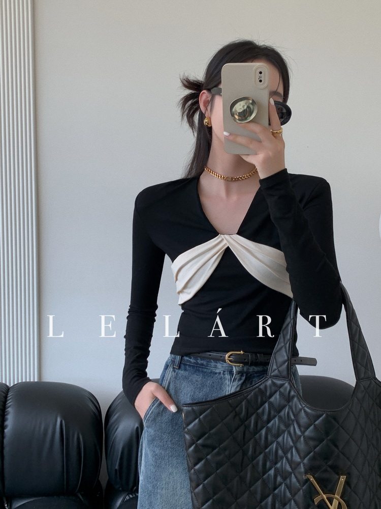 Model wearing a black long-sleeve top with a white twisted front detail and holding a quilted black handbag