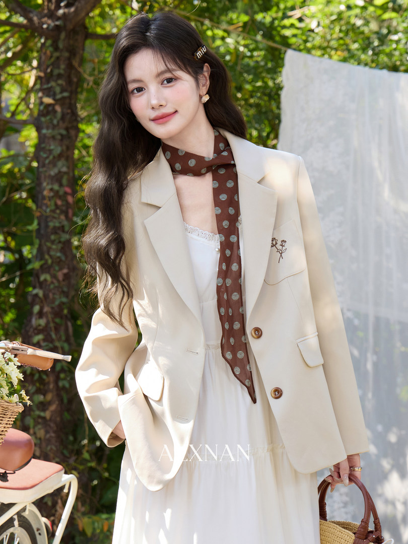 Woman wearing a cream blazer over a white dress with a polka-dot scarf outdoors