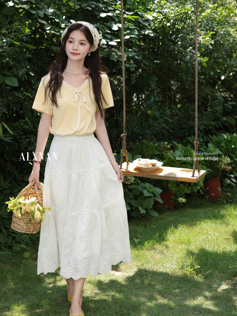 Woman wearing a pale yellow top and white skirt in a garden setting