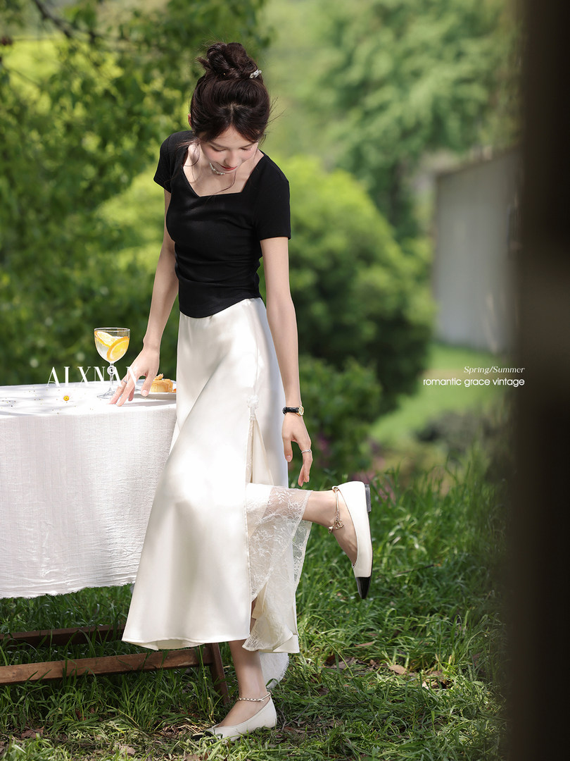 Woman wearing a black top with a white satin skirt and cream flats outdoors