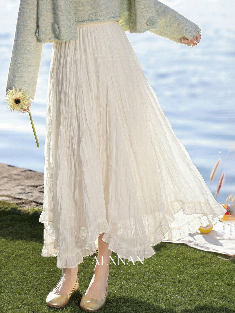 Model wearing a flowing white pleated skirt with a light knit sweater and gold flats outdoors
