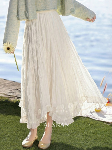 Model wearing a flowing white pleated skirt with a light knit sweater and gold flats outdoors