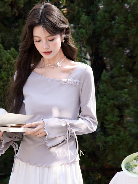 Model wearing a light gray long-sleeve feminine top with floral details