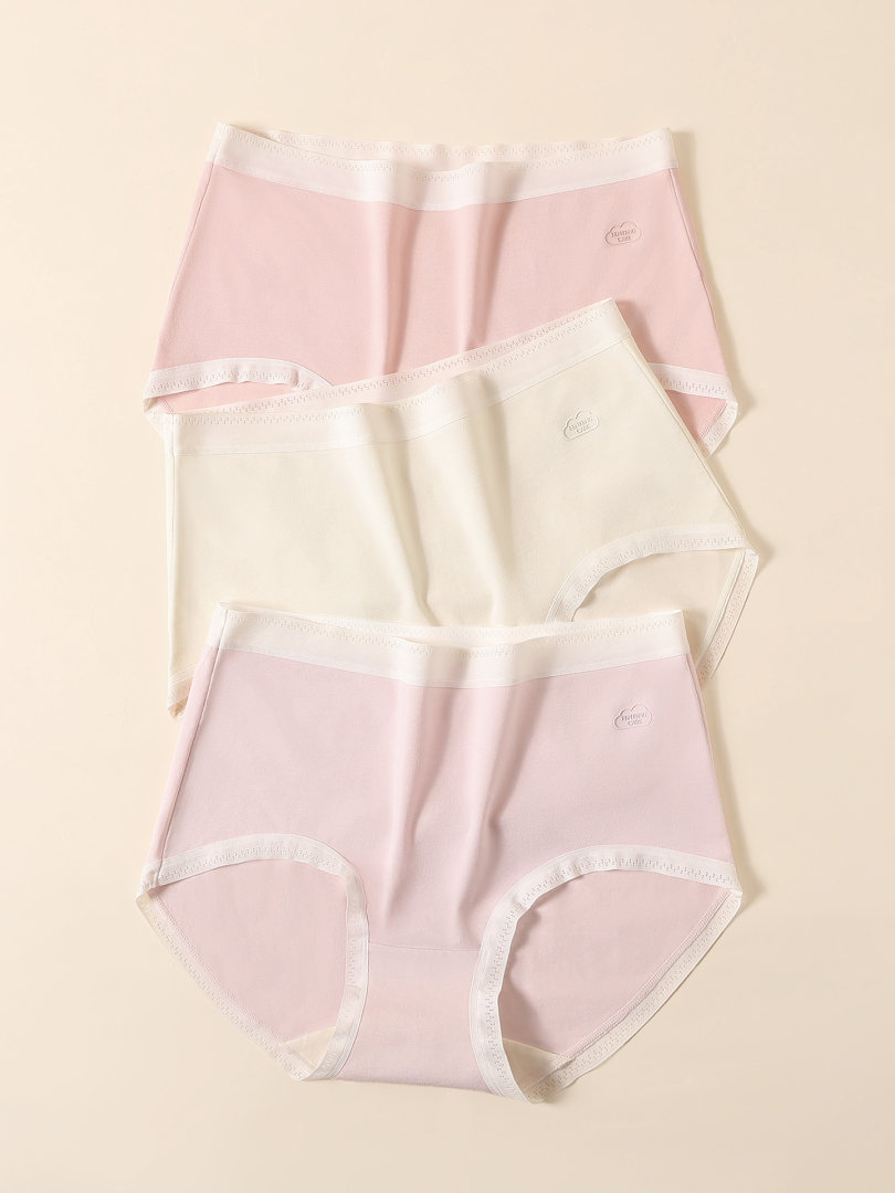Three pairs of pastel women's briefs laid flat on a beige background