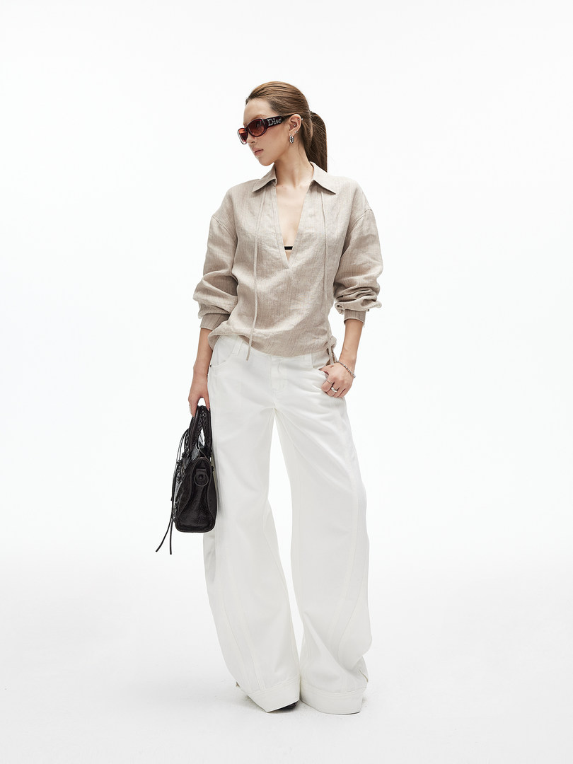 Model wearing a beige linen shirt with white wide-leg pants and a black handbag