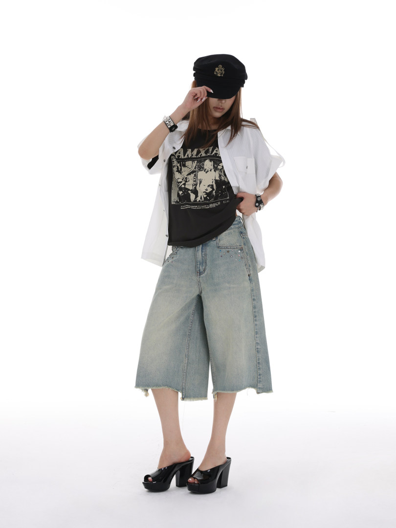 Model wearing a black cap, graphic tee, oversized white shirt, wide-leg denim shorts, and black platform heels
