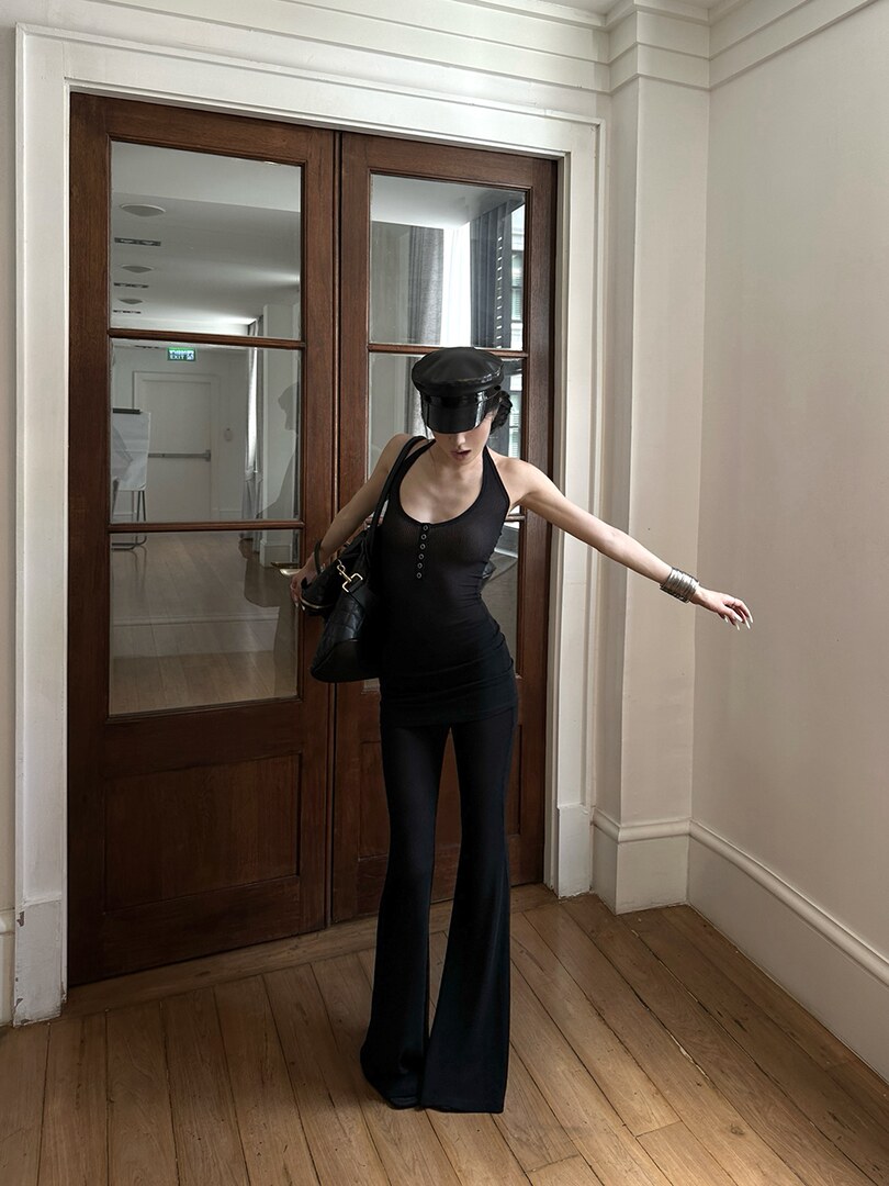 Model wearing a black fitted tank top and flared pants with a black handbag