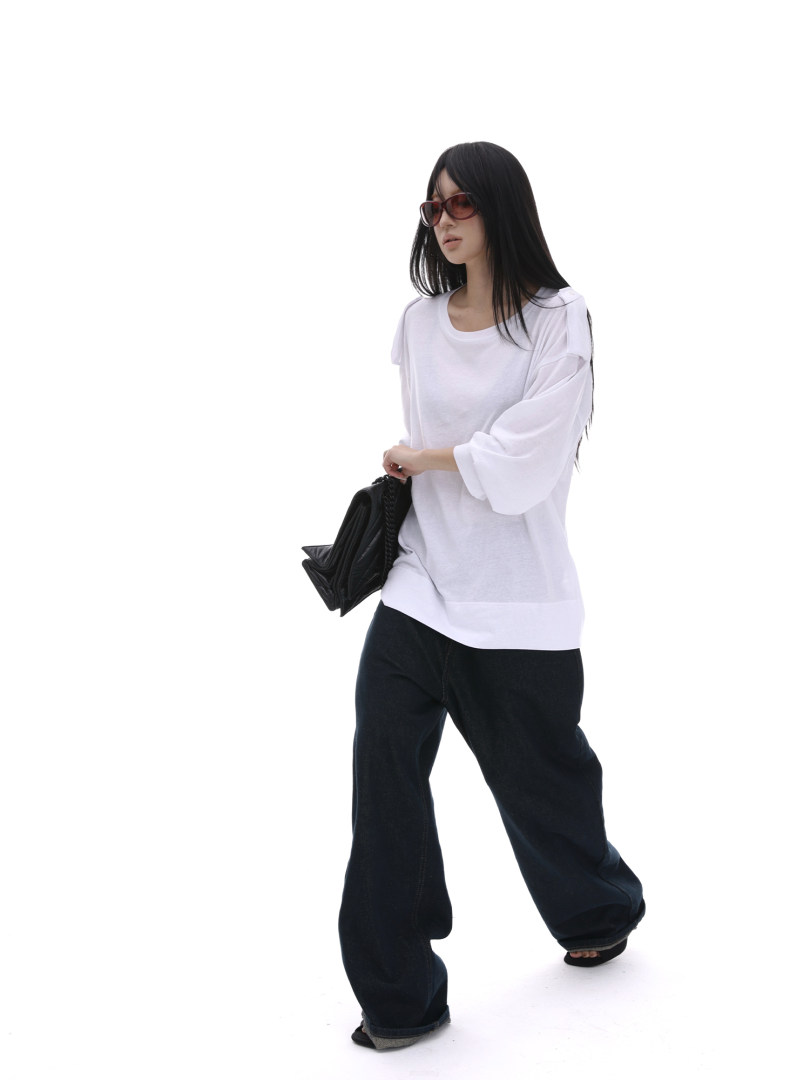 Model wearing a white oversized top and black wide-leg pants with a black handbag