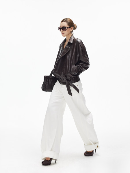 Fashion model wearing a black leather jacket with white wide-leg pants, sunglasses, handbag, and heels