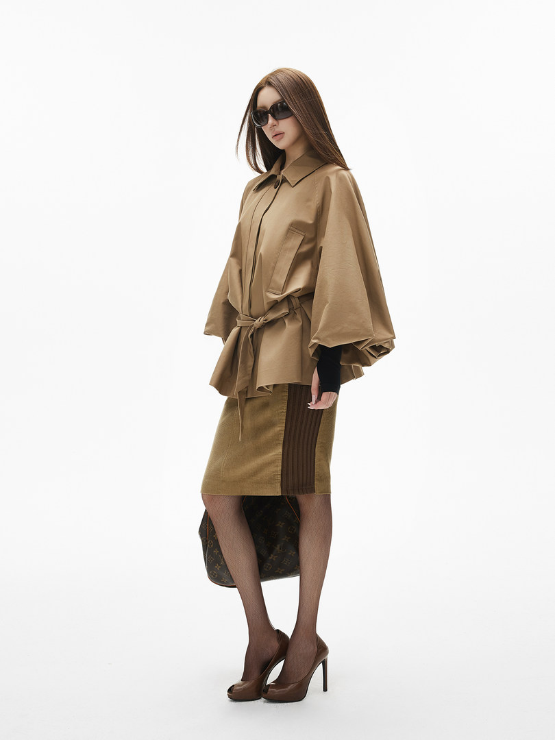 Fashion model wearing a beige belted top with matching skirt and heels on a white background