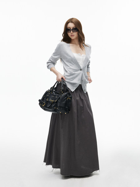 Model wearing a gray cardigan with a white top, long dark skirt, and black handbag