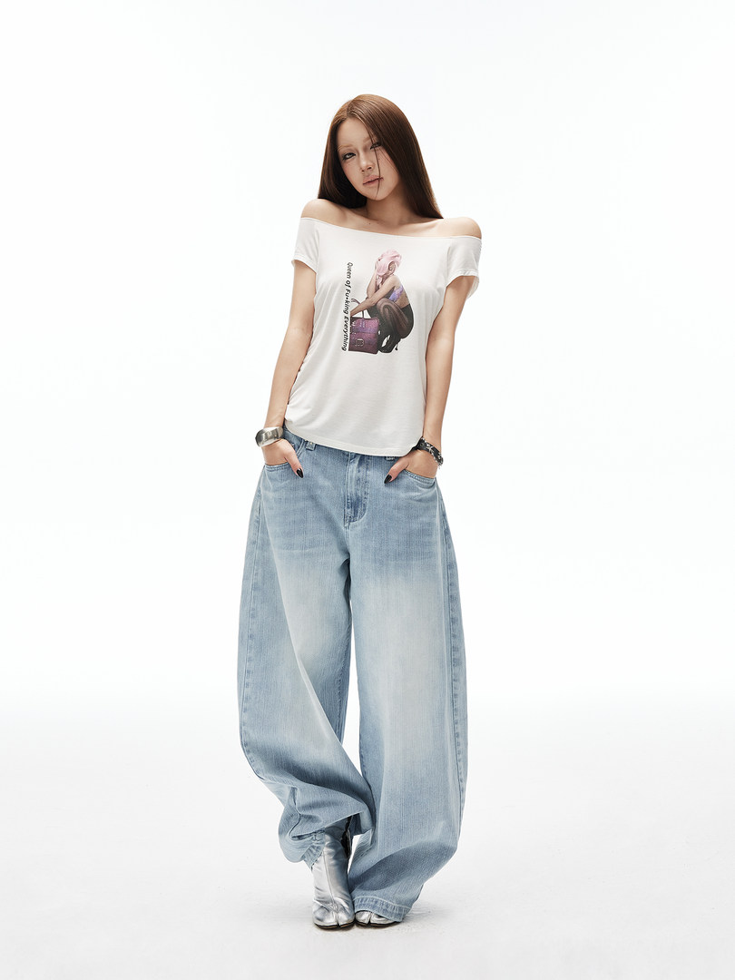 Model wearing a white graphic off-shoulder top with baggy light-wash jeans and silver boots