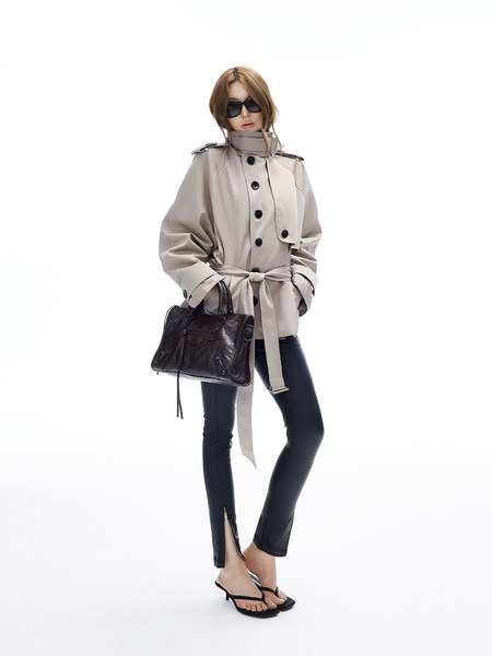 Fashion model wearing a beige trench coat with black pants, sandals, and a black handbag