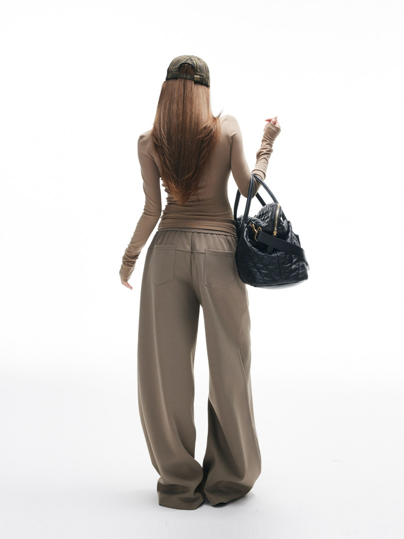 Model wearing a brown long-sleeve top and wide-leg pants with a black quilted handbag
